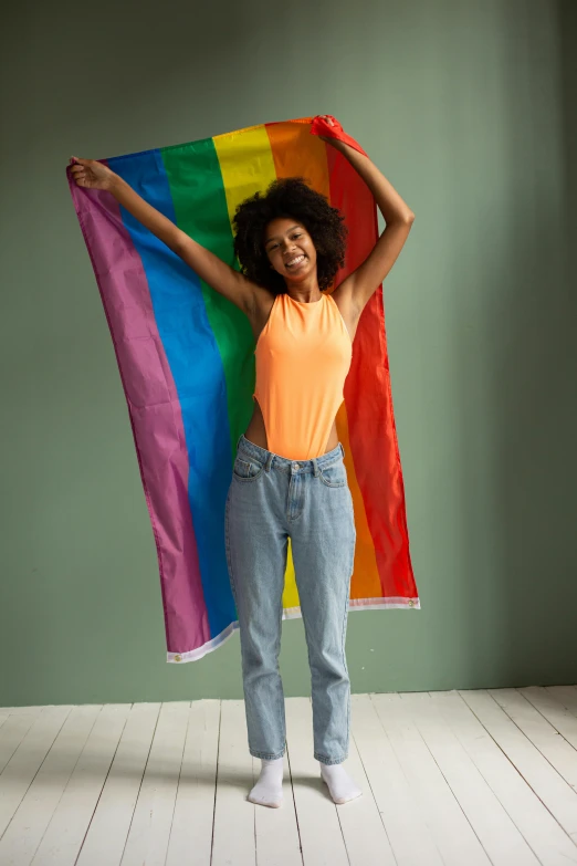 a woman holding a rainbow flag in a room, trending on pexels, wearing a shirt and a jean, ashteroth, standing triumphant and proud, solid background