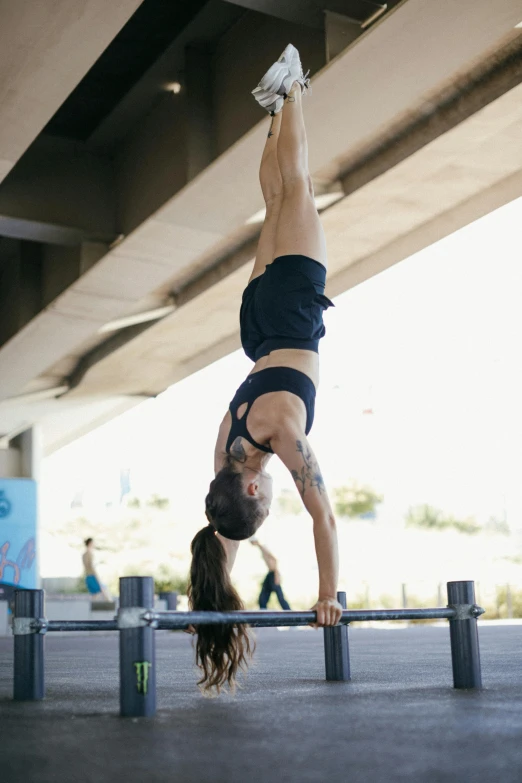 a woman doing a handstand in a parking lot, a portrait, unsplash, carrying two barbells, bridge, low quality photo, square