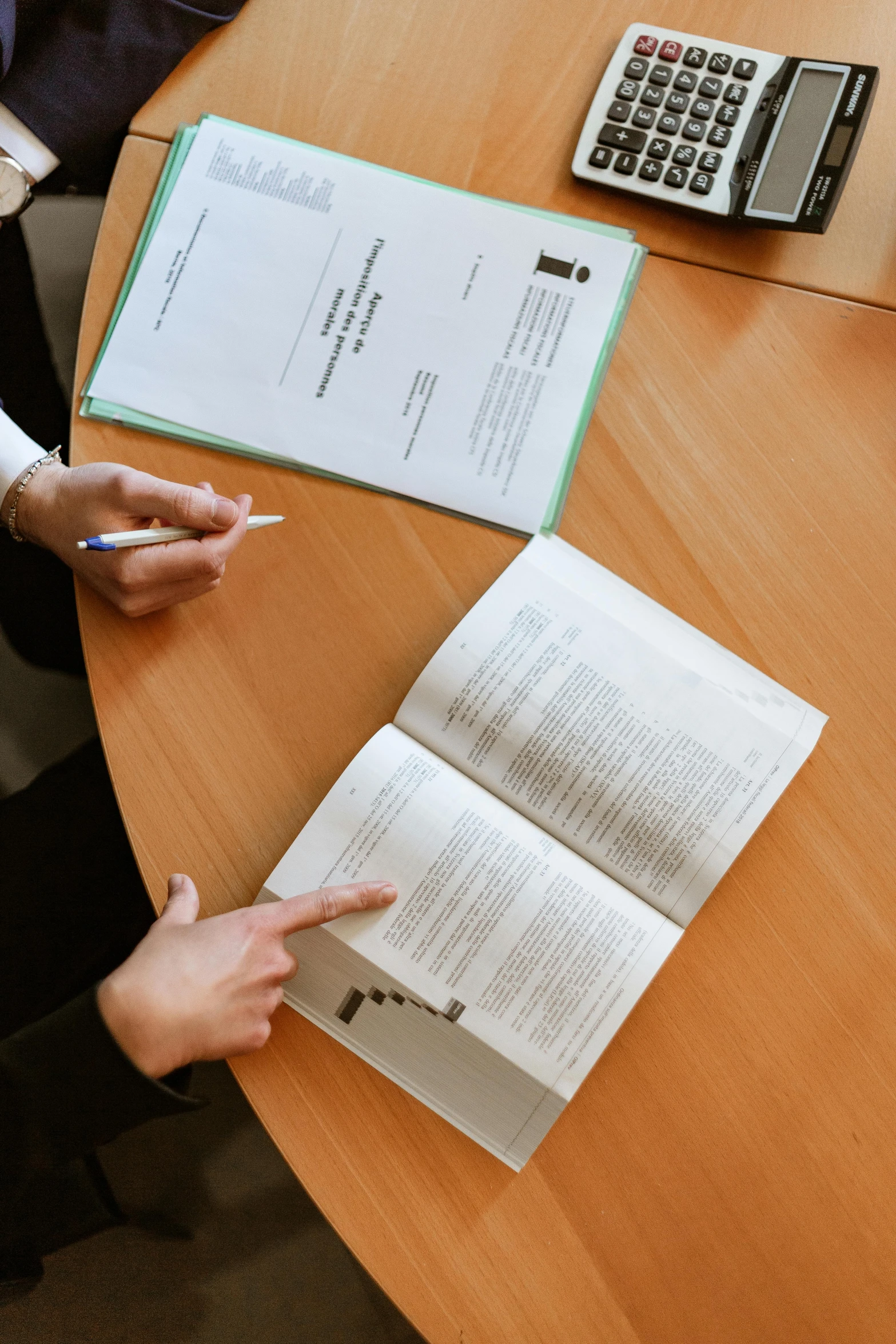 two people sitting at a table with papers and a calculator, by Matthias Stom, pexels contest winner, with pointing finger, library books, taken on iphone 14 pro, brochure