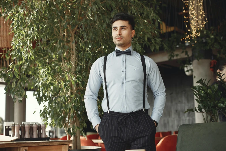 a man standing in a restaurant wearing suspenders and a bow tie, inspired by Ramon Pichot, khyzyl saleem, grey, medium-shot, wearing only pants