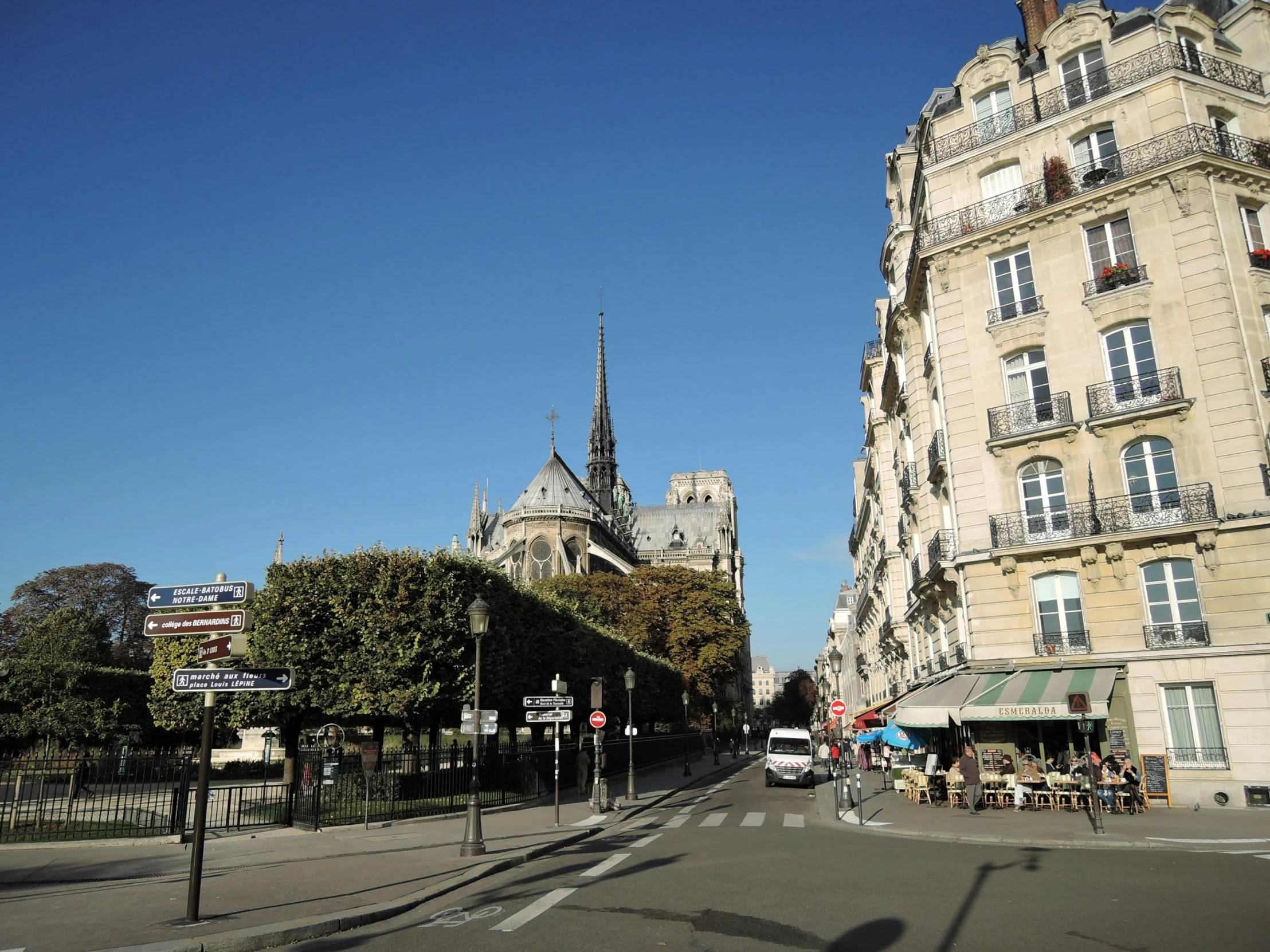 a street filled with lots of traffic next to tall buildings, an album cover, paris school, cathedral in the background, clear blue skies, 2022 photograph, square