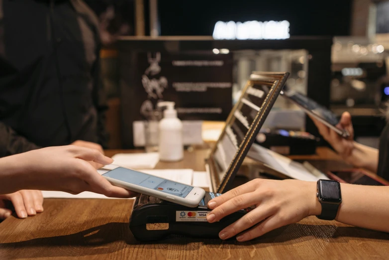 a group of people standing around a wooden table, at checkout, holding a very advance phone, thumbnail, insanly detailed