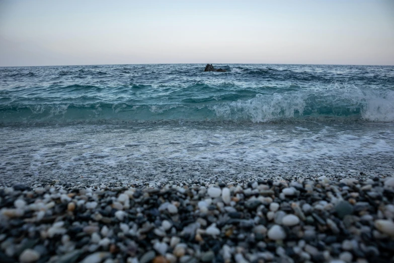 a person riding a surfboard on top of a rocky beach, by Francesco Furini, unsplash, realism, greece, pebbles, early evening, 2000s photo