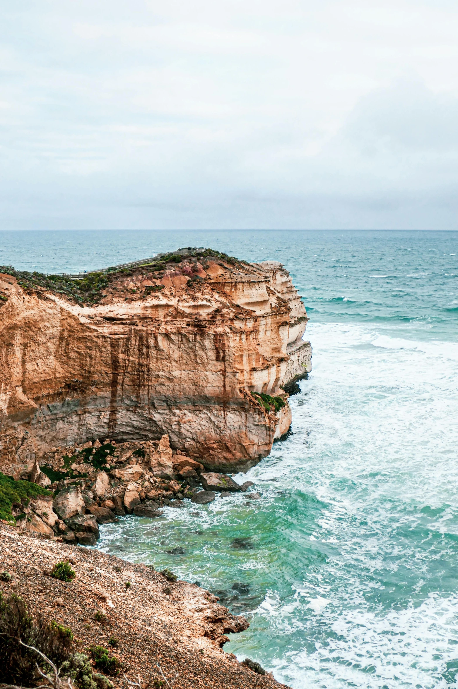 a man standing on top of a cliff next to the ocean, coastal cliffs, sandstone, overcast day, slide show