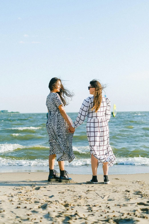 two women standing on a beach holding hands, by Julia Pishtar, happening, cute checkerboard sundress, wearing a luxurious silk robe, gen z, sailor clothing