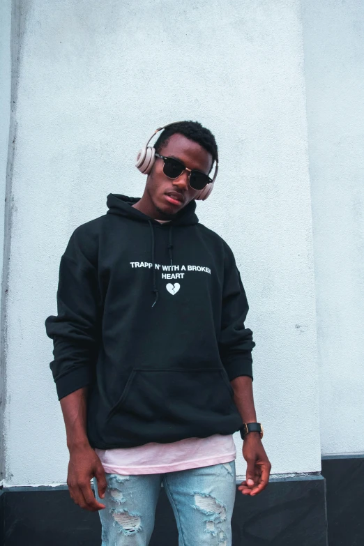 a man standing on a skateboard in front of a building, an album cover, trending on unsplash, hoody, black and white with hearts, wearing sunglasses, teddy fresh