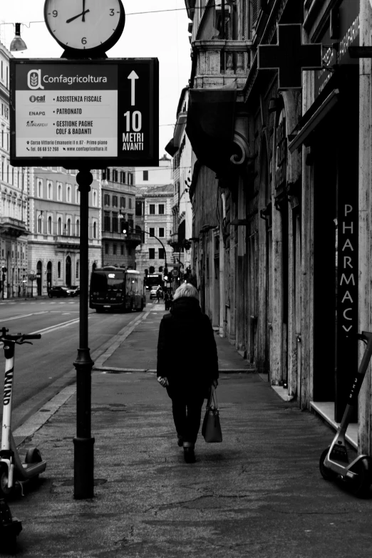 a black and white photo of a person walking down a street, a black and white photo, by Agnolo Gaddi, street signs, an old lady, photograph of the city street, of an old man