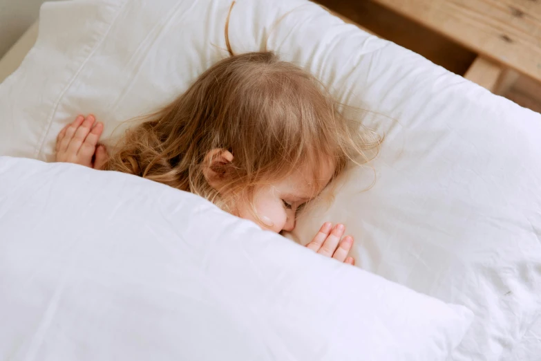 a little girl that is laying in a bed, by Alice Mason, pexels contest winner, hibernation capsule close-up, white pillows, asleep, thumbnail