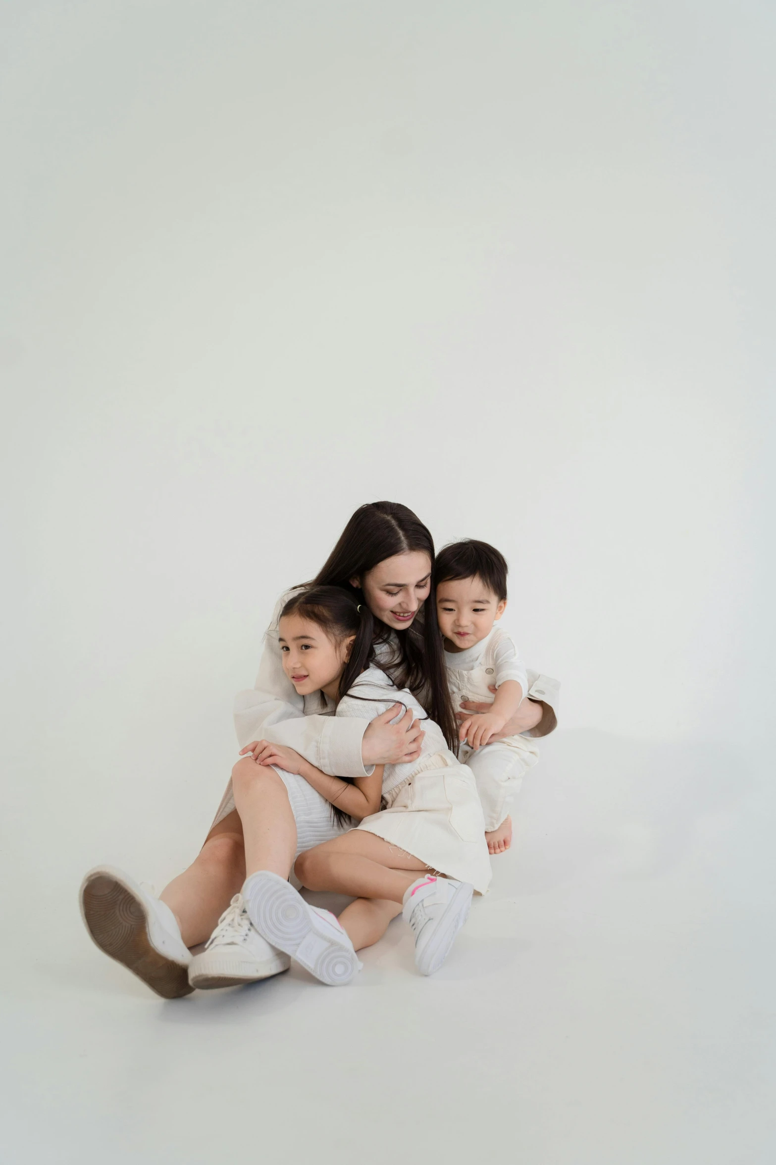 a woman and two children sitting next to each other, a picture, inspired by Li Di, pexels contest winner, in front of white back drop, light cream and white colors, instagram picture, hugging her knees