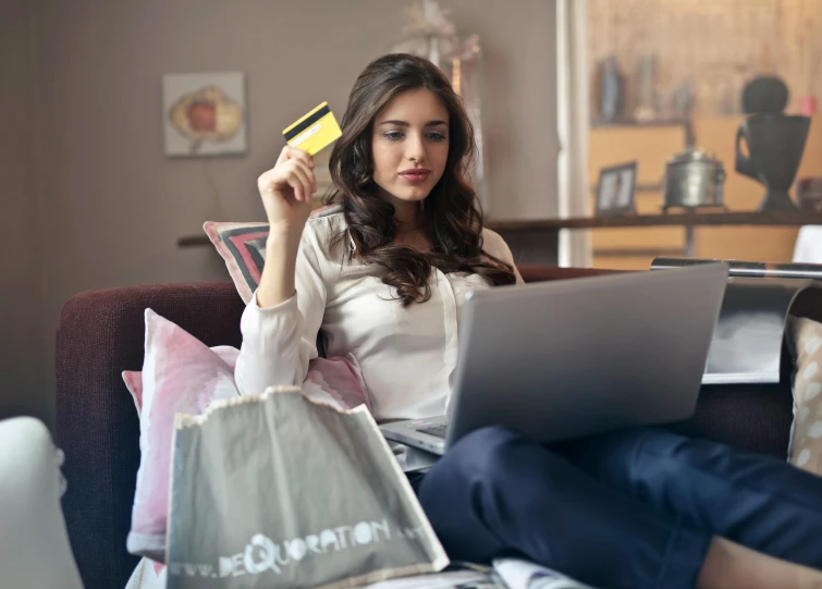 a woman sitting on a couch holding a credit card, by Julia Pishtar, pexels, figuration libre, shopping groceries, laptop, australian, then another