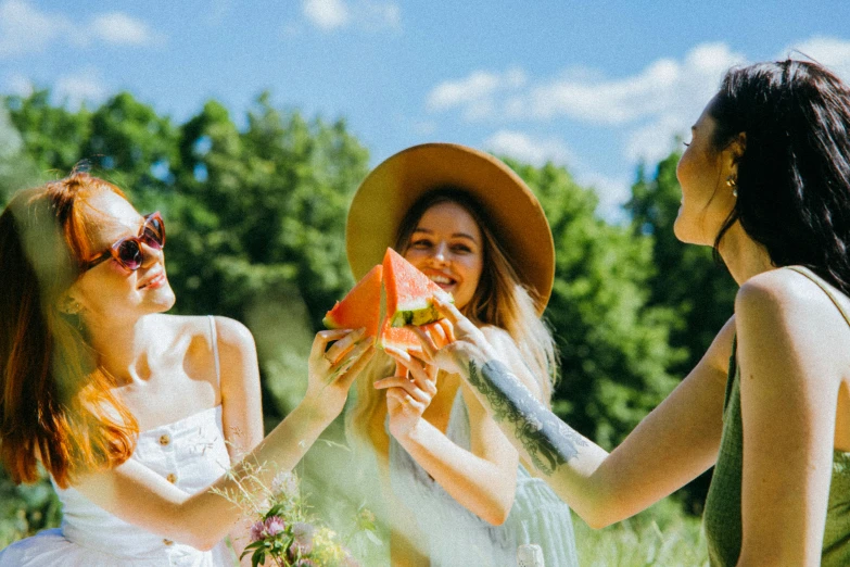 three women eating slices of watermelon in a field, by Julia Pishtar, pexels contest winner, giving gifts to people, sydney sweeney, with hat, 3 young and beautiful women