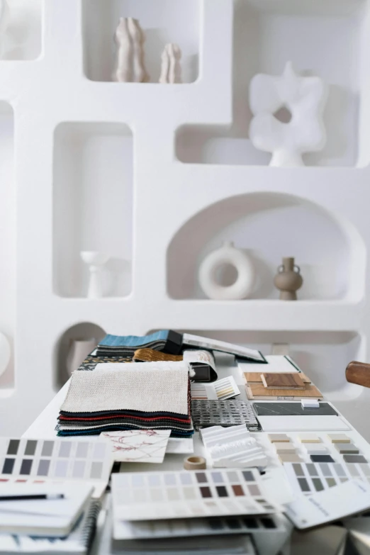 a table that has a bunch of papers on it, a still life, inspired by Ricardo Bofill, minimalism, fabrics, white ceramic shapes, greek setting, architect studio