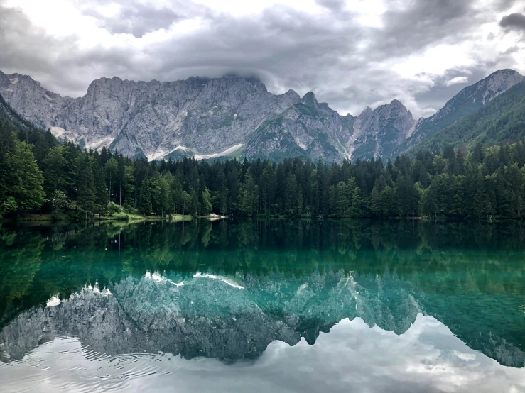 a body of water with mountains in the background, by Emma Andijewska, pexels contest winner, mirror lake, dark green water, multiple stories, dolomites in the background
