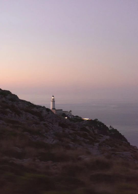 a lighthouse sitting on top of a hill next to the ocean, muted lights, ibiza, movie filmstill, set photo