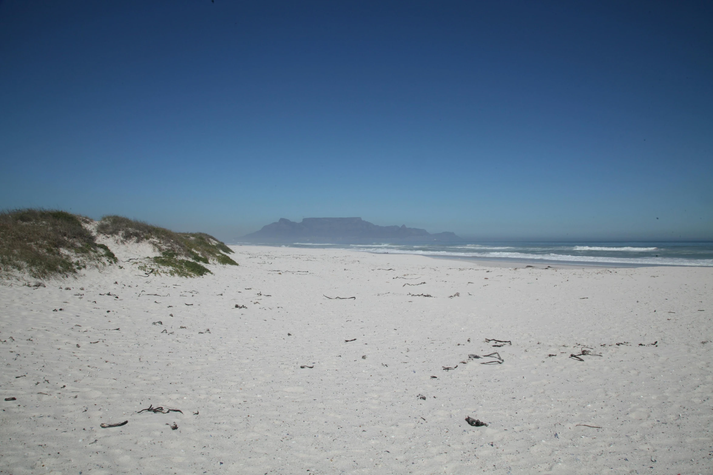 a sandy beach with a mountain in the distance, a picture, cape, white, white beaches, beach on the outer rim