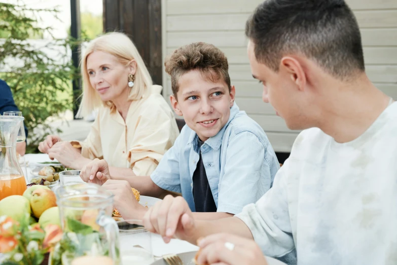 a group of people sitting around a dinner table, boy with neutral face, school curriculum expert, profile image, al fresco