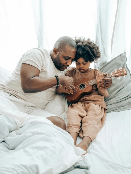 a man sitting on top of a bed next to a little girl, pexels contest winner, ukulele, profile image, african american, holding an epée