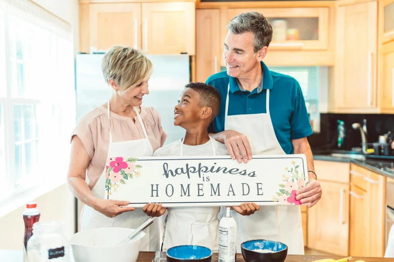 a man and two women holding a sign in a kitchen, by John Backderf, pexels contest winner, happiness!, clematis theme banner, husband wife and son, made of glazed