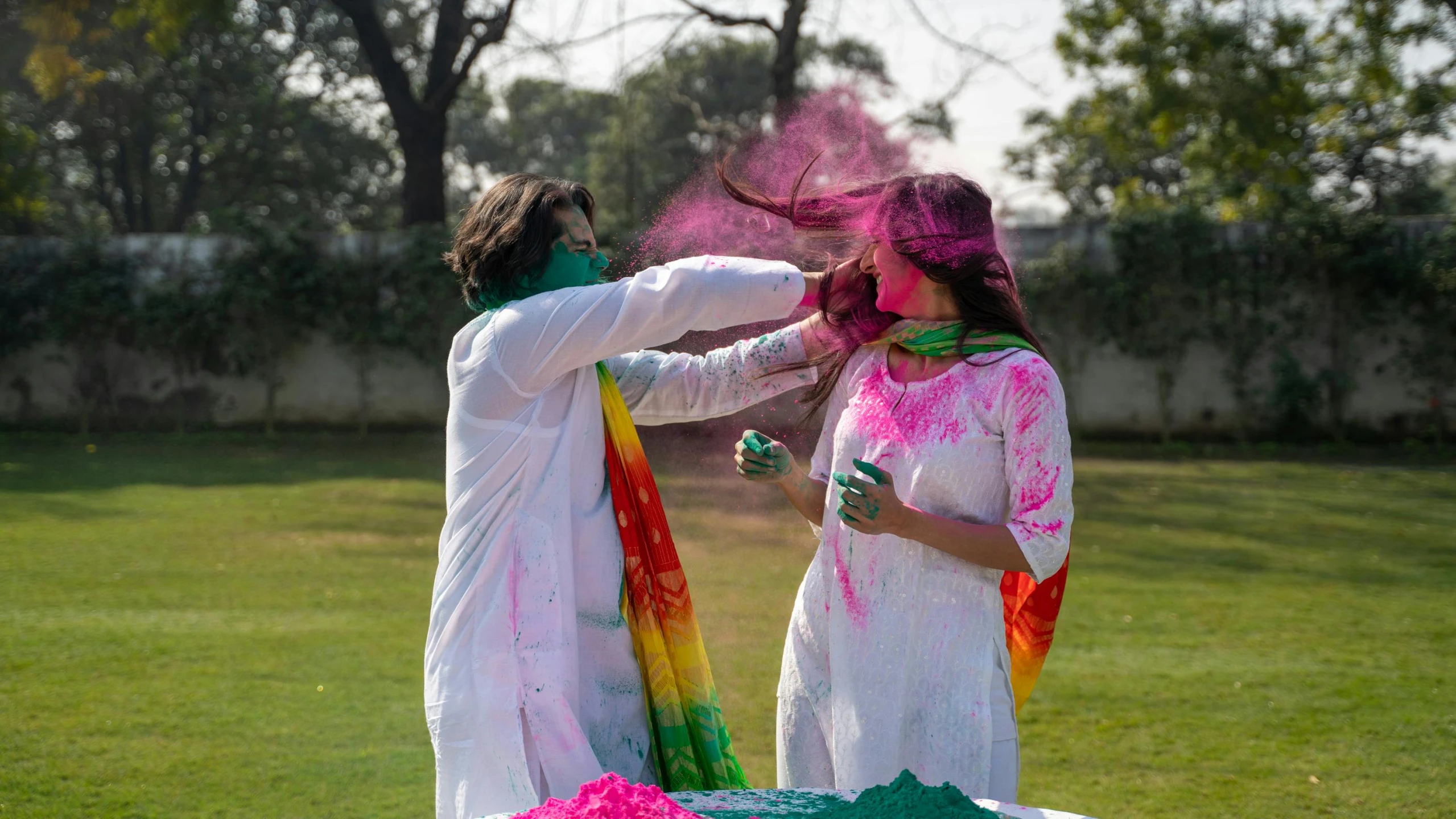 a couple of women standing on top of a lush green field, a colorized photo, pexels contest winner, color field, holi festival of rich color, her face is coated in a white, wearing a kurta, casting a multi colored spell