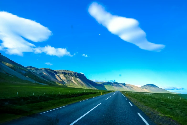 a car driving down a road with mountains in the background, by Hallsteinn Sigurðsson, pexels contest winner, hurufiyya, blue sky and green grassland, square, college, low - angle