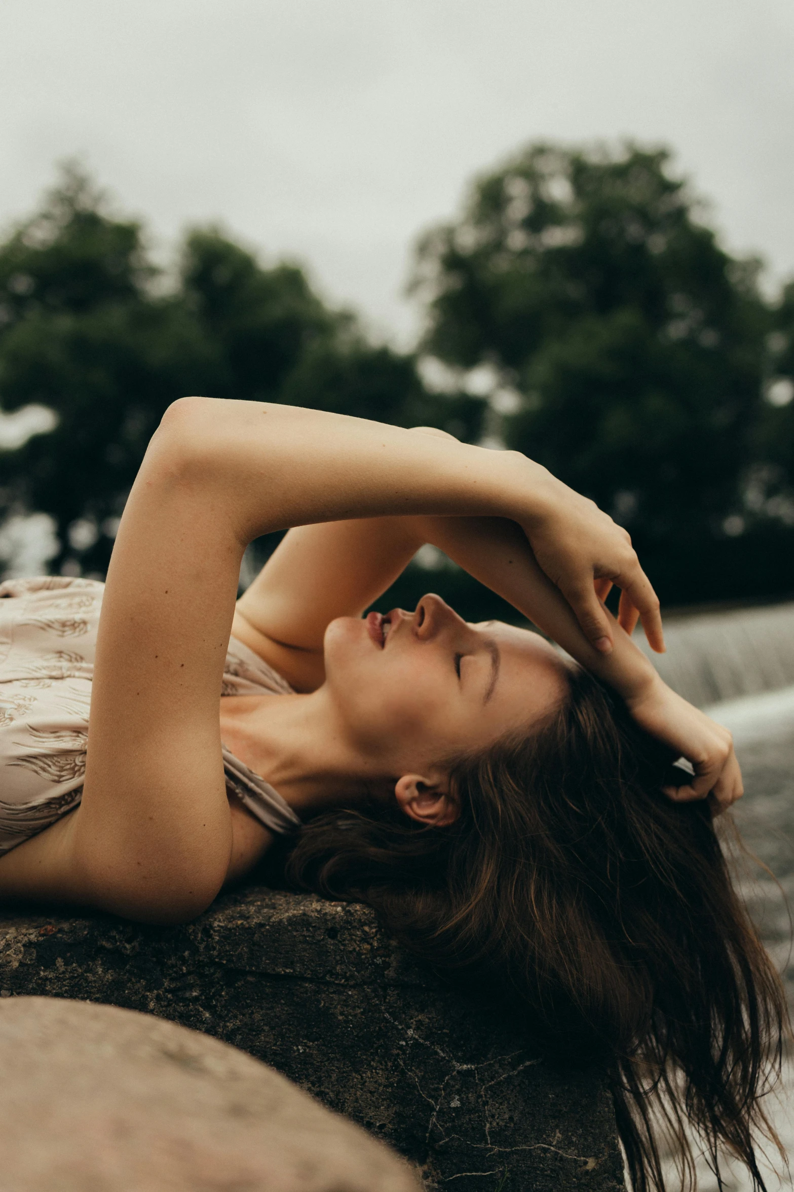 a woman laying on top of a rock next to a body of water, inspired by Elsa Bleda, pexels contest winner, renaissance, attractive face and body, blowing hair, head tilted downward, low quality photo