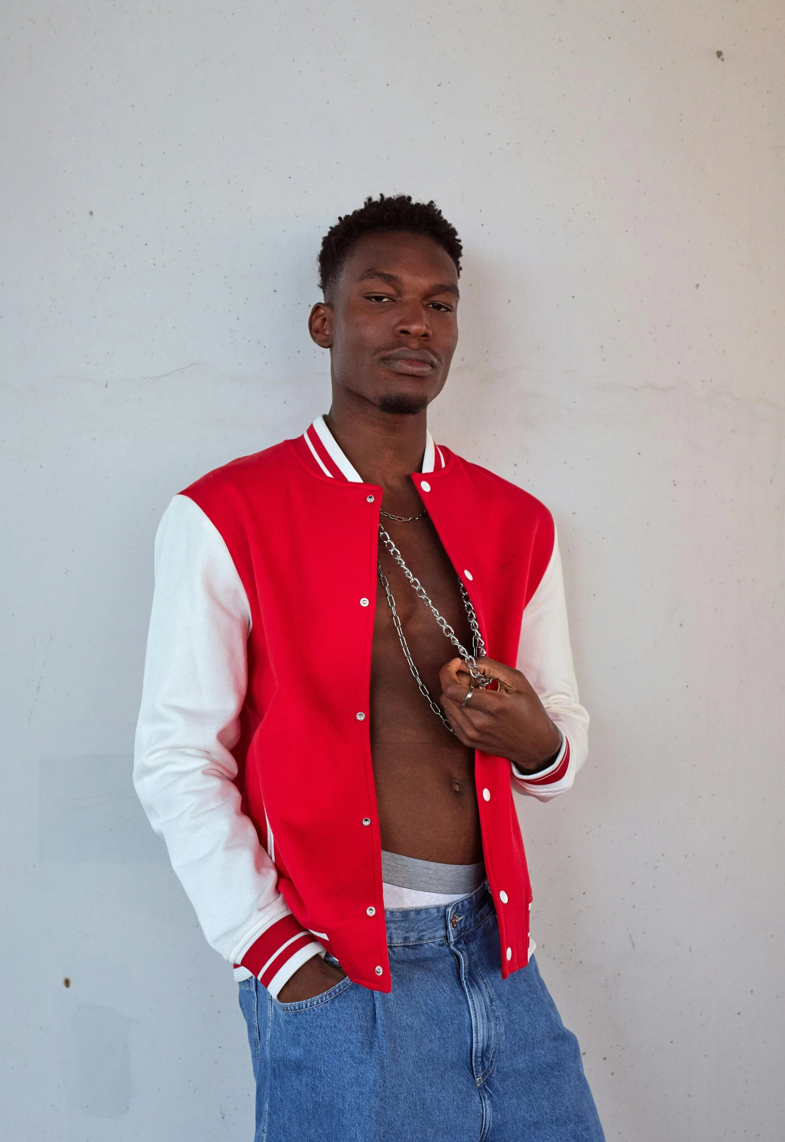 a man standing in front of a white wall, an album cover, by Stokely Webster, trending on unsplash, wearing red attire, wearing a bomber jacket, model posing, promo image