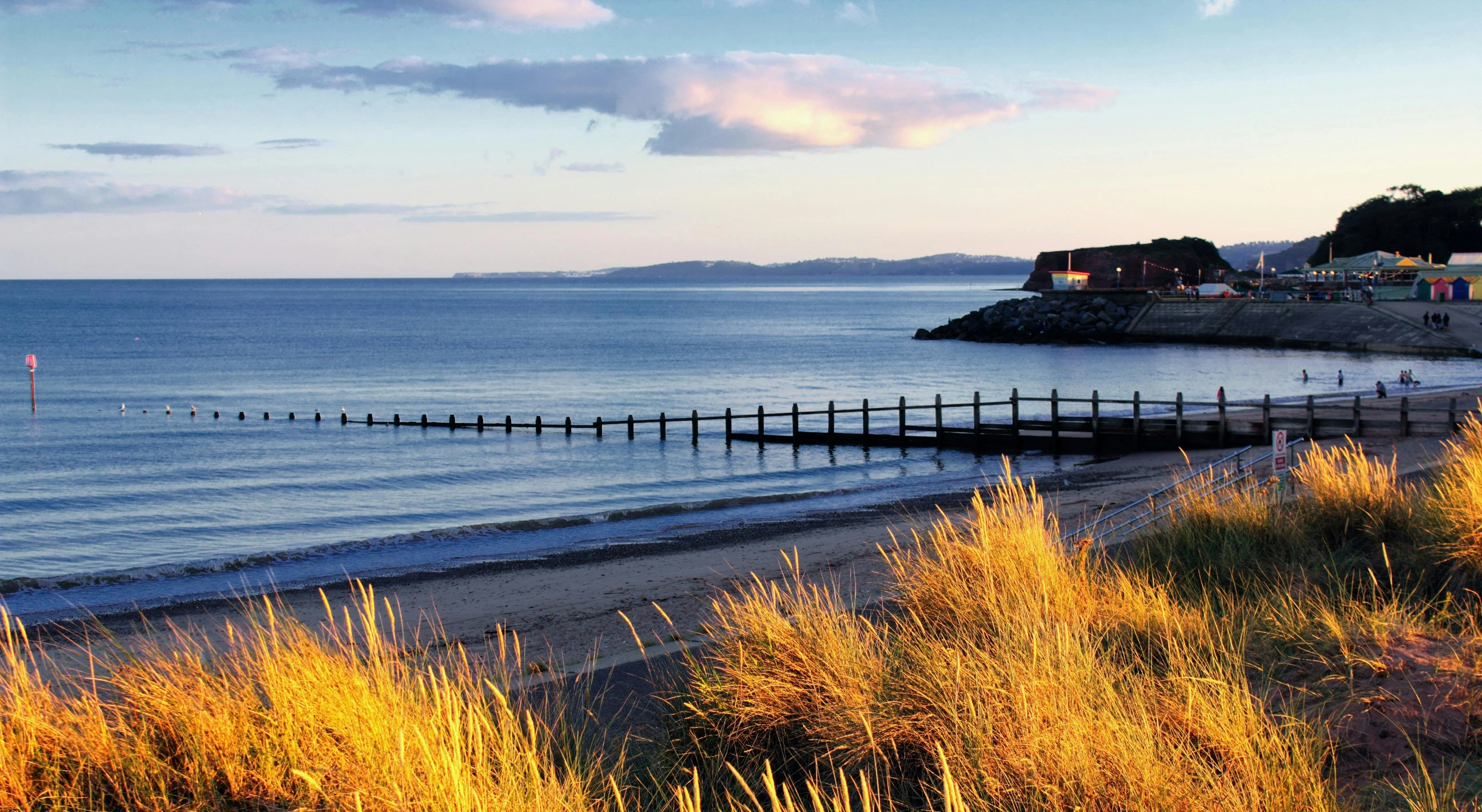 a sandy beach next to a body of water, which shows a beach at sunset, autumn colours, wood pier and houses, sand banks