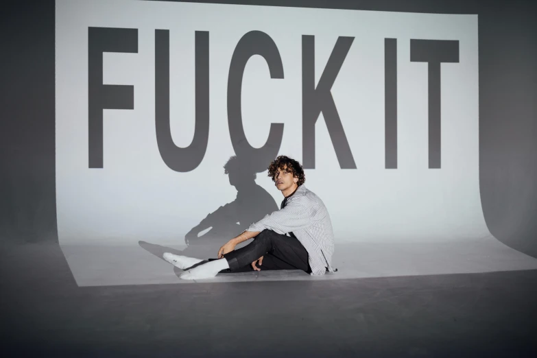 a man sitting on the ground in front of a sign, inspired by Fei Danxu, graffiti, finn wolfhard, nick knight, show it, press shot