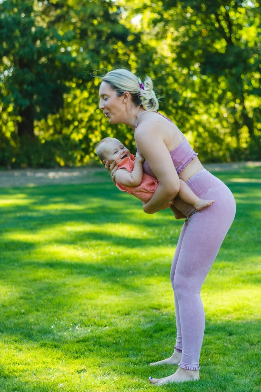 a woman holding a baby in her arms, an album cover, pexels contest winner, happening, stretching her legs on the grass, with abs, avatar image, heath clifford