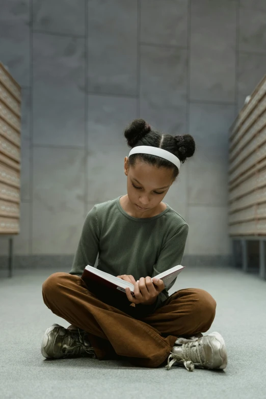 a young girl sitting on the floor reading a book, by Greg Spalenka, pexels contest winner, renaissance, brown skinned, in school hallway, paul barson, greta thunberg