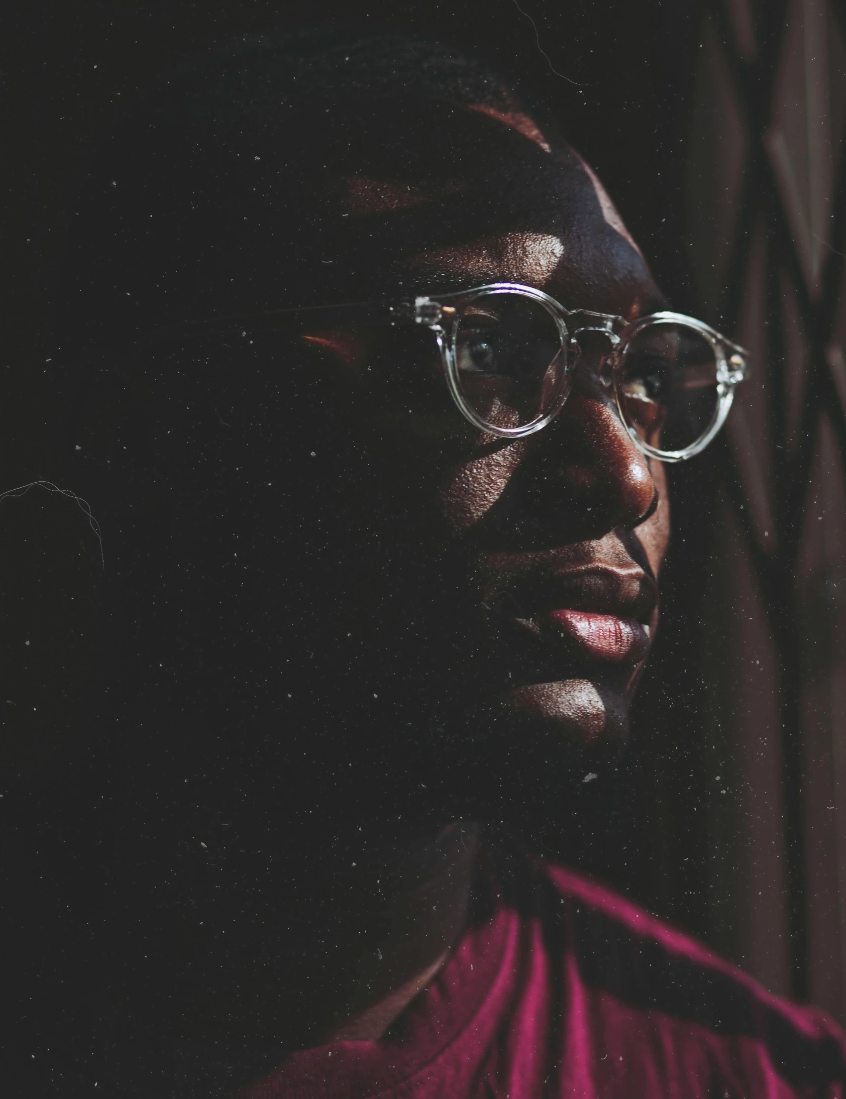 a close up of a person wearing glasses, an album cover, by Stokely Webster, moody hazy lighting, looking from side, low quality photo, ( ( dark skin ) )