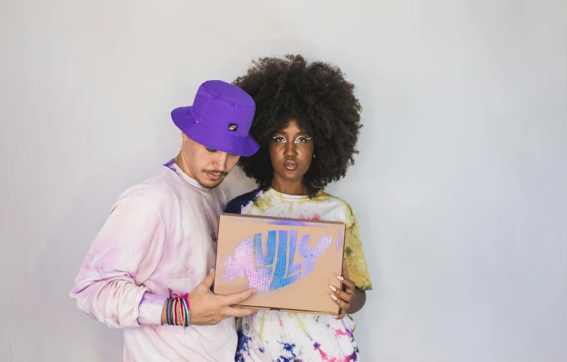 a man and woman standing next to each other holding a box, unsplash, afrofuturism, wearing a purple cap, rainbow mycelium, official product photo, blue fedora
