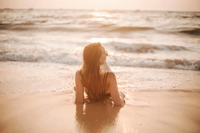 a woman sitting on top of a sandy beach next to the ocean, pexels contest winner, flowing backlit hair, half submerged in heavy sand, profile image, people in beach