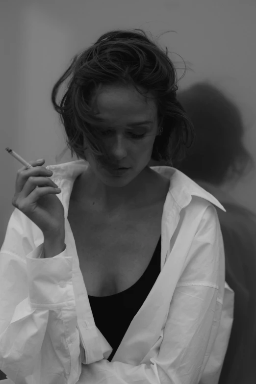 a black and white photo of a woman smoking a cigarette, inspired by Nan Goldin, tumblr, hyperrealism, wearing a white button up shirt, alicia vikander, devon cady-lee, ansel ]