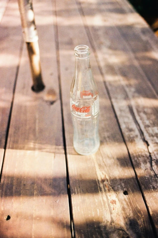a bottle sitting on top of a wooden table, inspired by Dorothy Coke, unsplash, translucent, soda, 1 9 6 0 s, picnic
