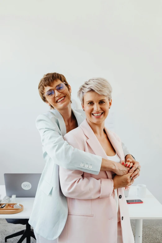 two women hugging each other in an office, a picture, pexels contest winner, in front of white back drop, looking confident, lesbian, collectors