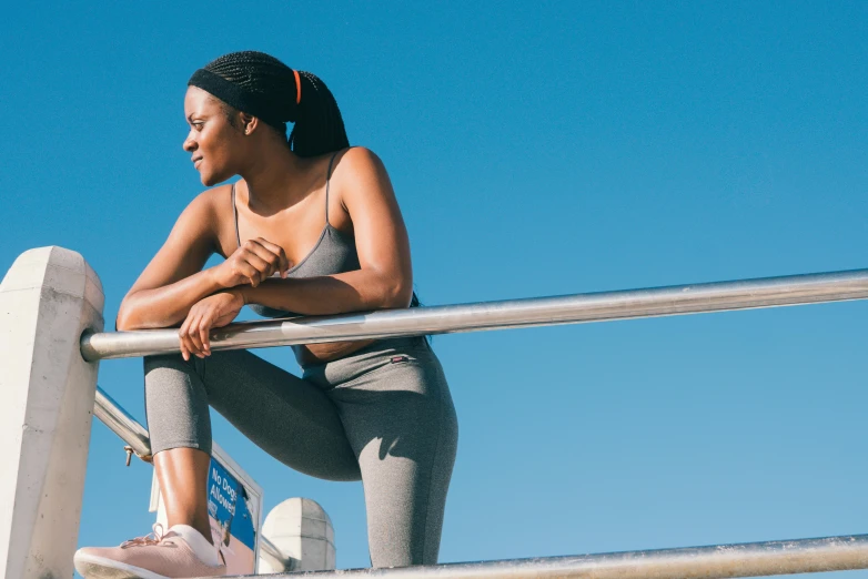 a woman sitting on top of a metal railing, trending on pexels, wearing fitness gear, clear blue skies, dark skinned, sweat and labour