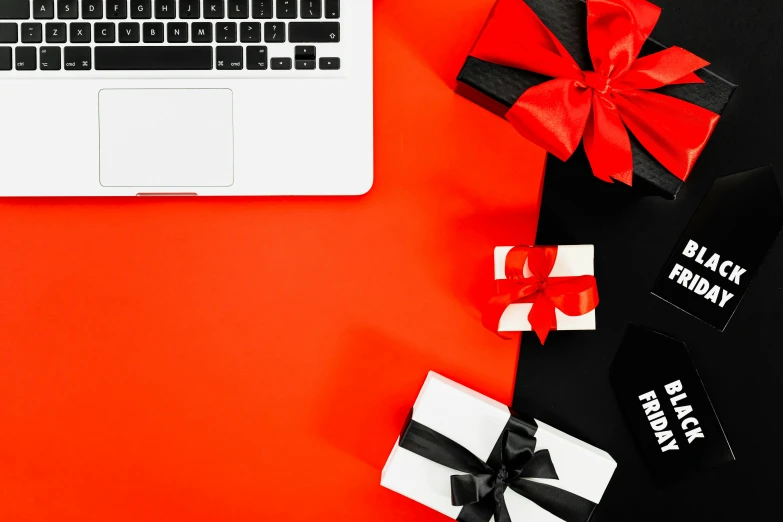 a laptop computer sitting on top of a desk next to a bunch of presents, by Julia Pishtar, pexels contest winner, black on red, flat lay, bows, black and orange colour palette