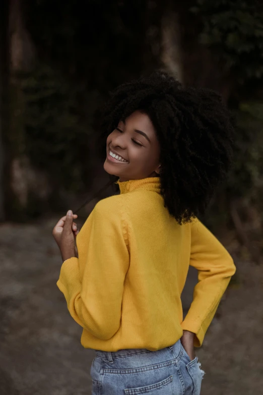 a woman standing in the middle of a dirt road, wavy hair yellow theme, wearing turtleneck, smiling playfully, portrait featured on unsplash