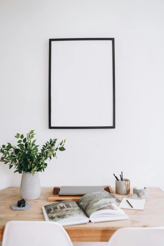 a picture frame sitting on top of a wooden table, a minimalist painting, trending on unsplash, whiteboard, white wall, dslr photo of a vase on a table, high quality photo