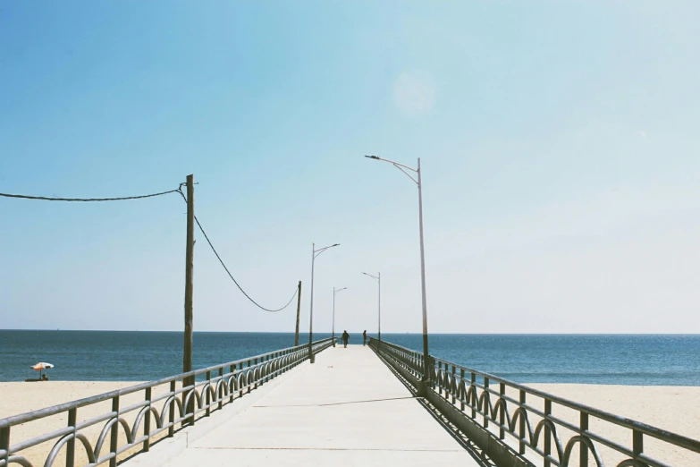 a bench sitting on top of a pier next to the ocean, by Carey Morris, pexels contest winner, minimalism, light blue clear sky, people walking in the distance, bridge, new jersey