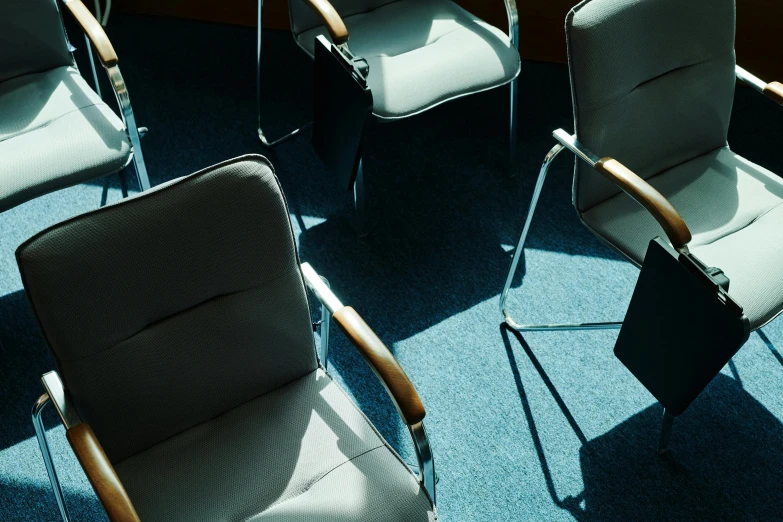 a group of chairs sitting on top of a blue carpet, by David Donaldson, trending on unsplash, modernism, softly shadowed, doctors office, shafts of sunlight in the centre, high-angle