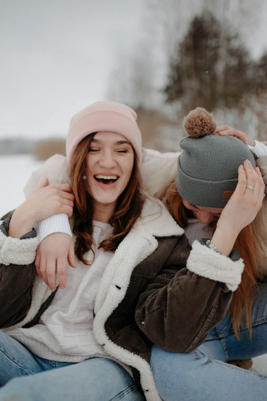 a couple of women sitting next to each other in the snow, trending on pexels, happening, beanie, excited russians, arm around her neck, half image