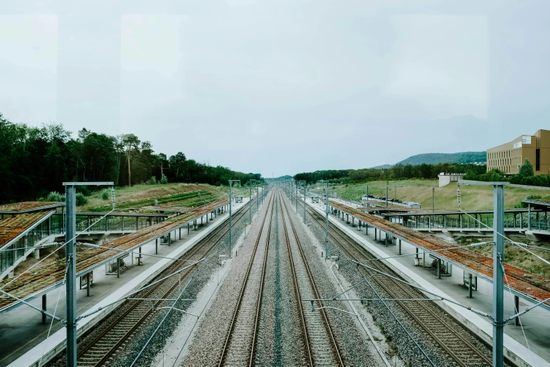 a train traveling down train tracks next to a lush green hillside, an album cover, inspired by Thomas Struth, unsplash, hyperrealism, symmetrical. sci - fi, sangsoo jeong, panorama view, terminals