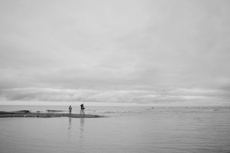 a couple of people that are standing in the water, a black and white photo, unsplash, minimalism, hd footage, slight overcast weather, hunting, near the seashore