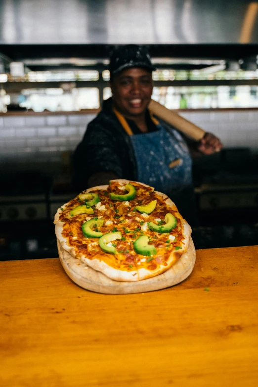 a pizza sitting on top of a wooden table, unmistakably kenyan, avocado, thumbnail, at the counter