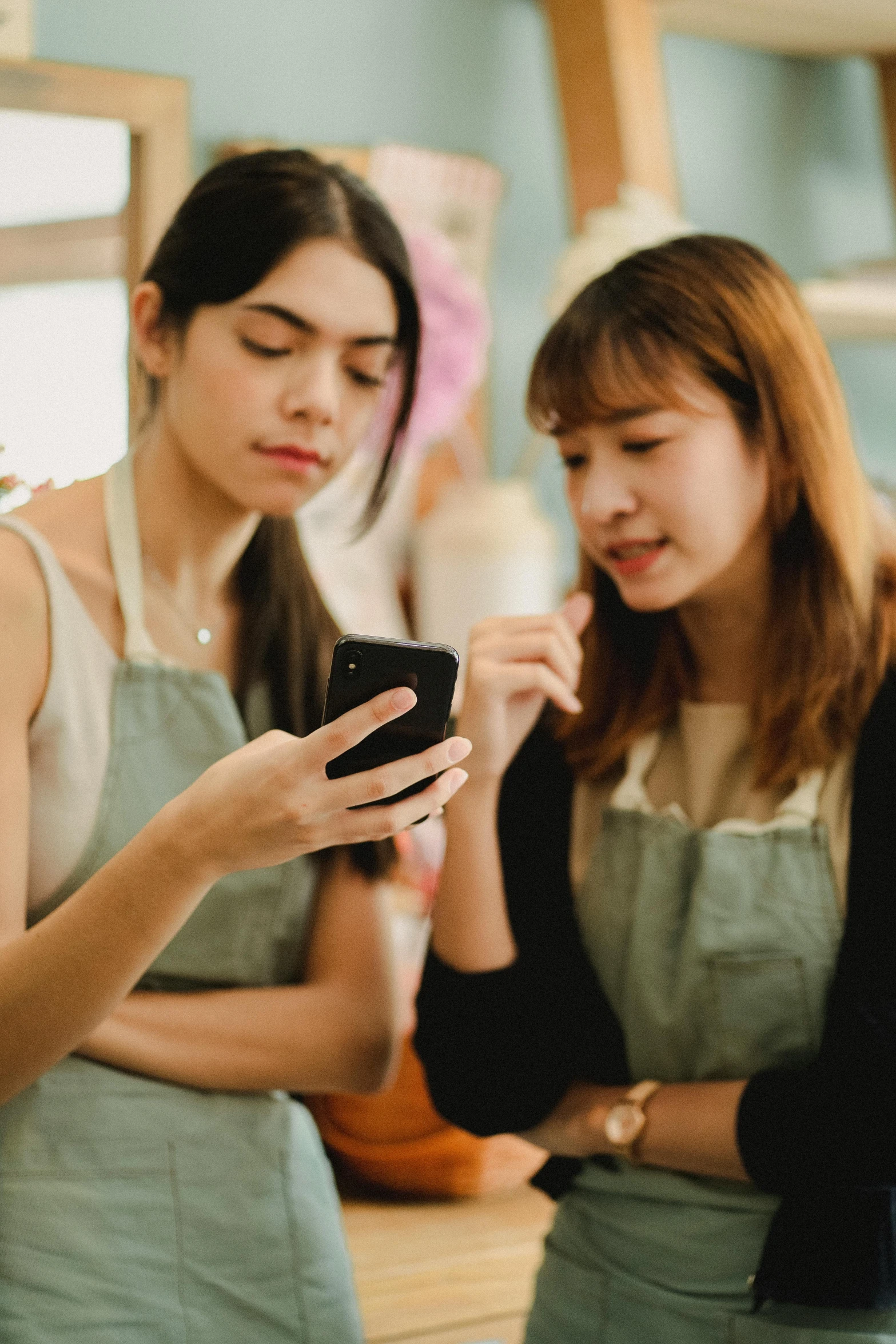 two women standing next to each other looking at a cell phone, trending on pexels, realism, south east asian with long, at the counter, etsy, a group of people