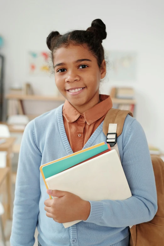 a young girl standing in a classroom holding a folder, shutterstock contest winner, happening, light-brown skin, carrying a saddle bag, holding a stack of books, brown and cyan color scheme