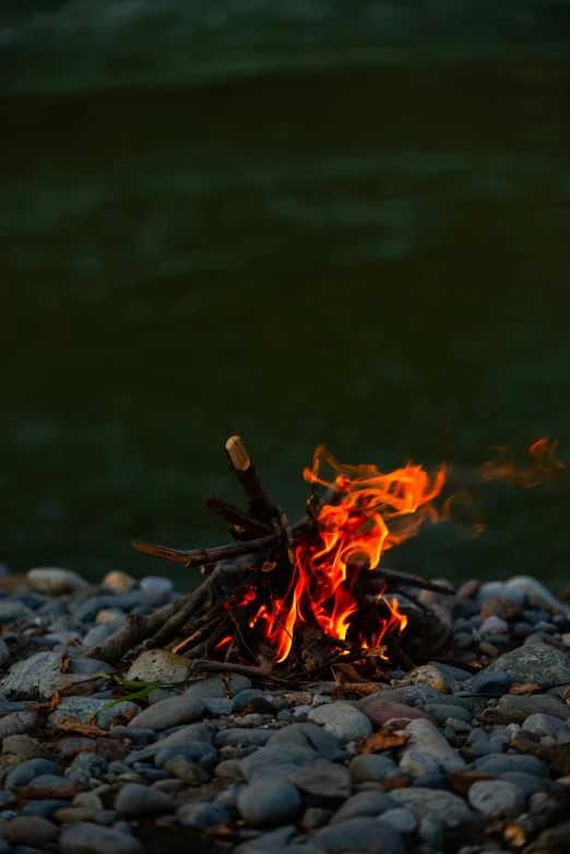 a campfire sitting on top of a rocky beach, on a riverbank, may 1 0, fires, headshot