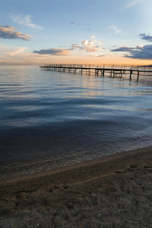 a large body of water sitting on top of a sandy beach, by Peter Churcher, boat dock, during sunset, beaches